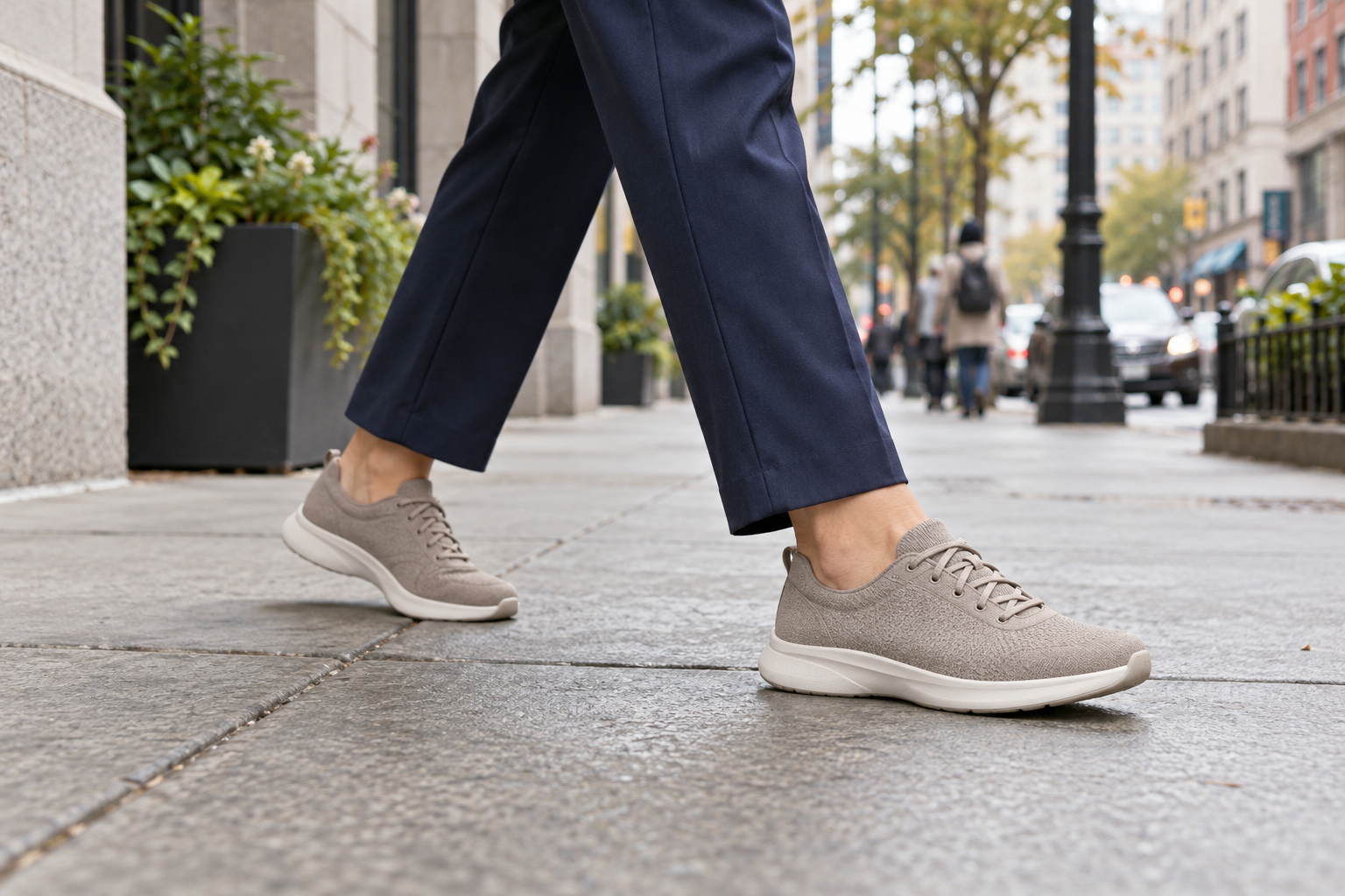 Woman walking along a city sidewalk in taupe low-profile walking shoes and navy trousers